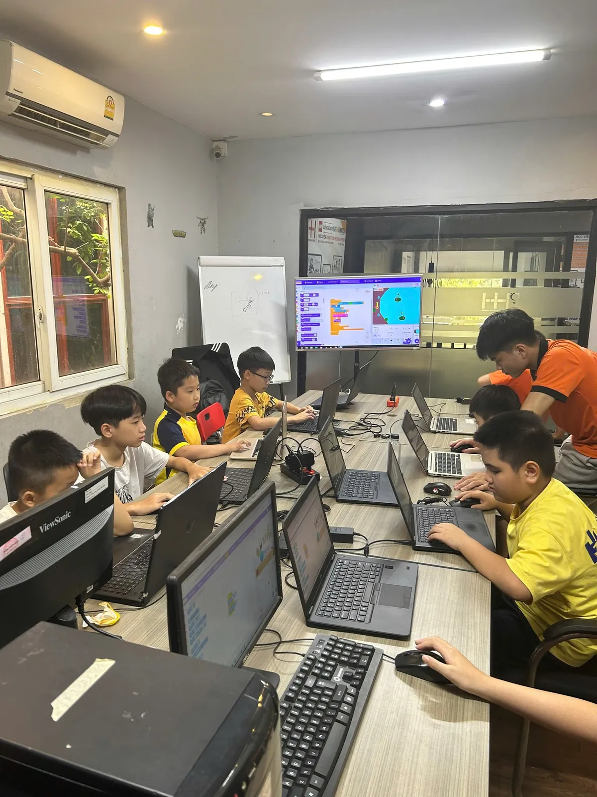 Phòng lập trình Scratch tại Học viện RHH: học sinh làm việc trên máy tính bàn, màn hình hiển thị giao diện lập trình kéo thả